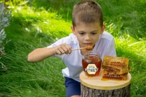 A jar of natural honey with a wooden dipper beside a glass of milk, fruits, and toast, symbolizing the health benefits of honey for kids’ growth, energy, and immunity.