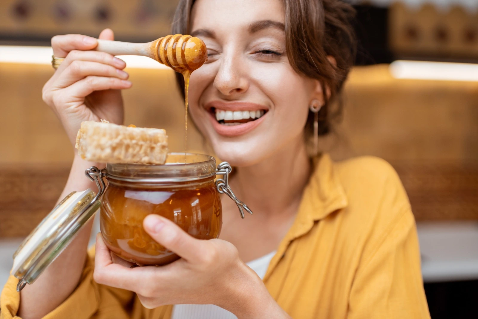 Woman enjoying raw honey, holding a jar with honeycomb and a wooden dipper, highlighting natural honey for women’s wellness and health.