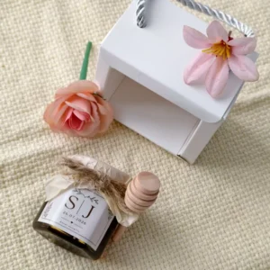 White gift box with wedding honey favours, a wooden dipper, and a pink flower.