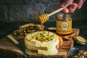 Honey dipper drizzling pure honey on cheese dish with Sidr honey jar for Honey and Cheese Pairings.