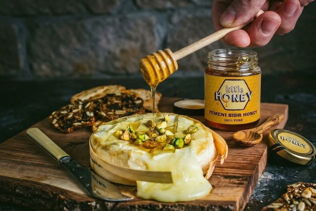 Honey dipper drizzling pure honey on cheese dish with Sidr honey jar for Honey and Cheese Pairings.